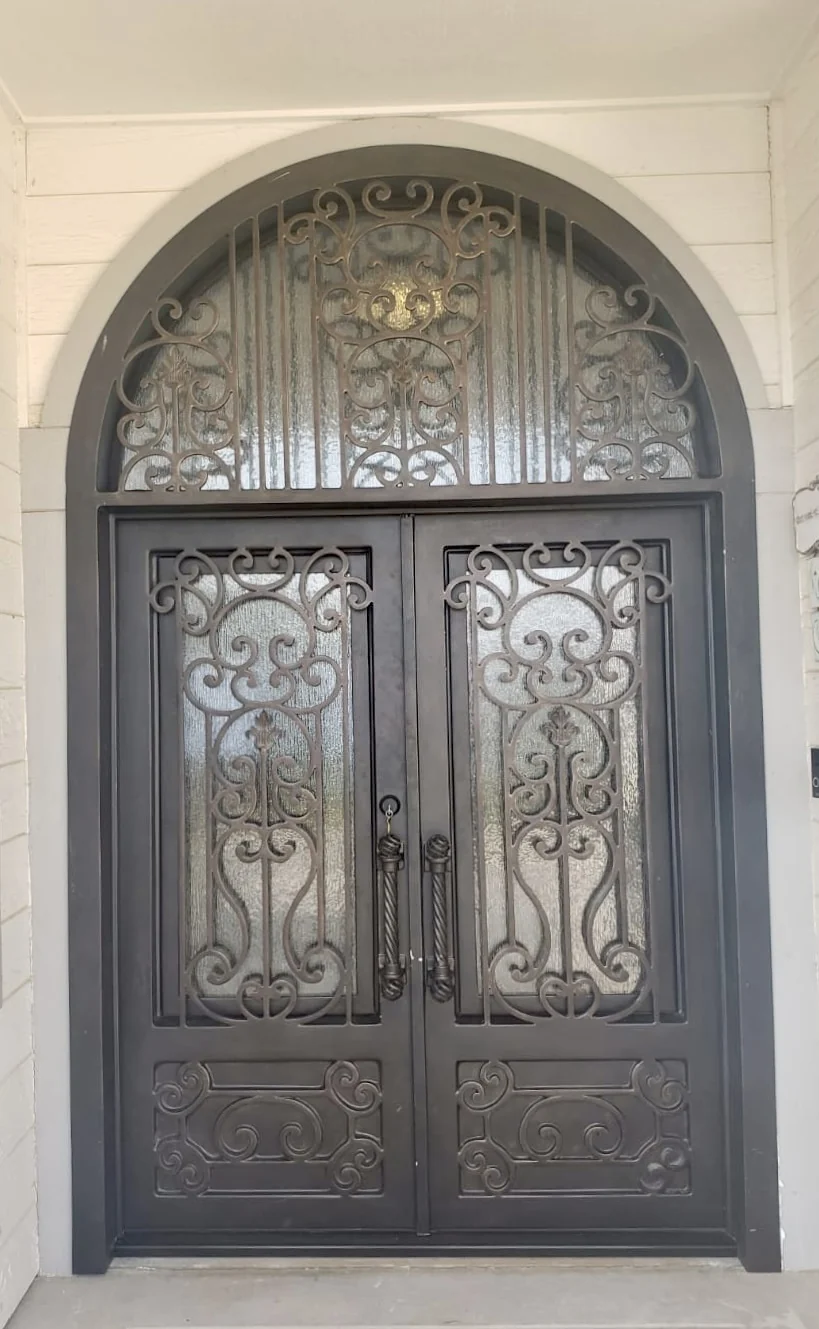 Grand arched iron double entry with dense scrollwork and ornamental transom